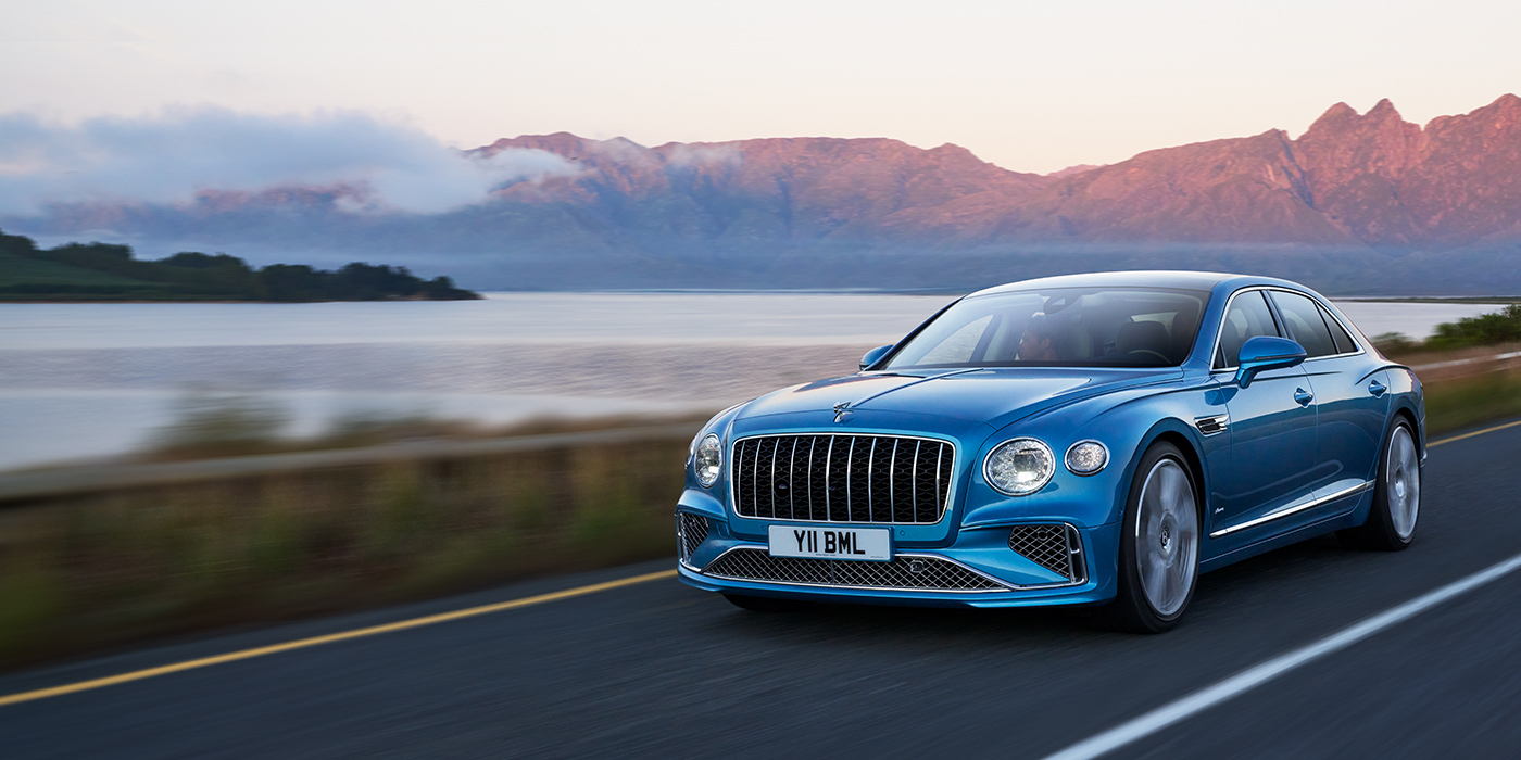 Bentley Lyon New Bentley Flying Spur Azure sedan in Light windsor blue paint by Mulliner, with 22 inch Azure wheels and chrome straight vaned grille driving on a mountain road