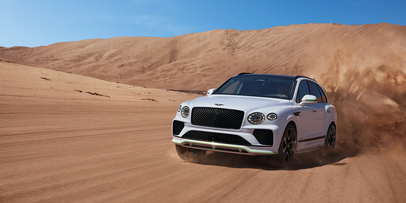 Bentley Lyon Bentley Bentayga Speed SUV front three quarter in Snow Quarts Pearlescent by Mulliner white paint driving dynamically through the desert
