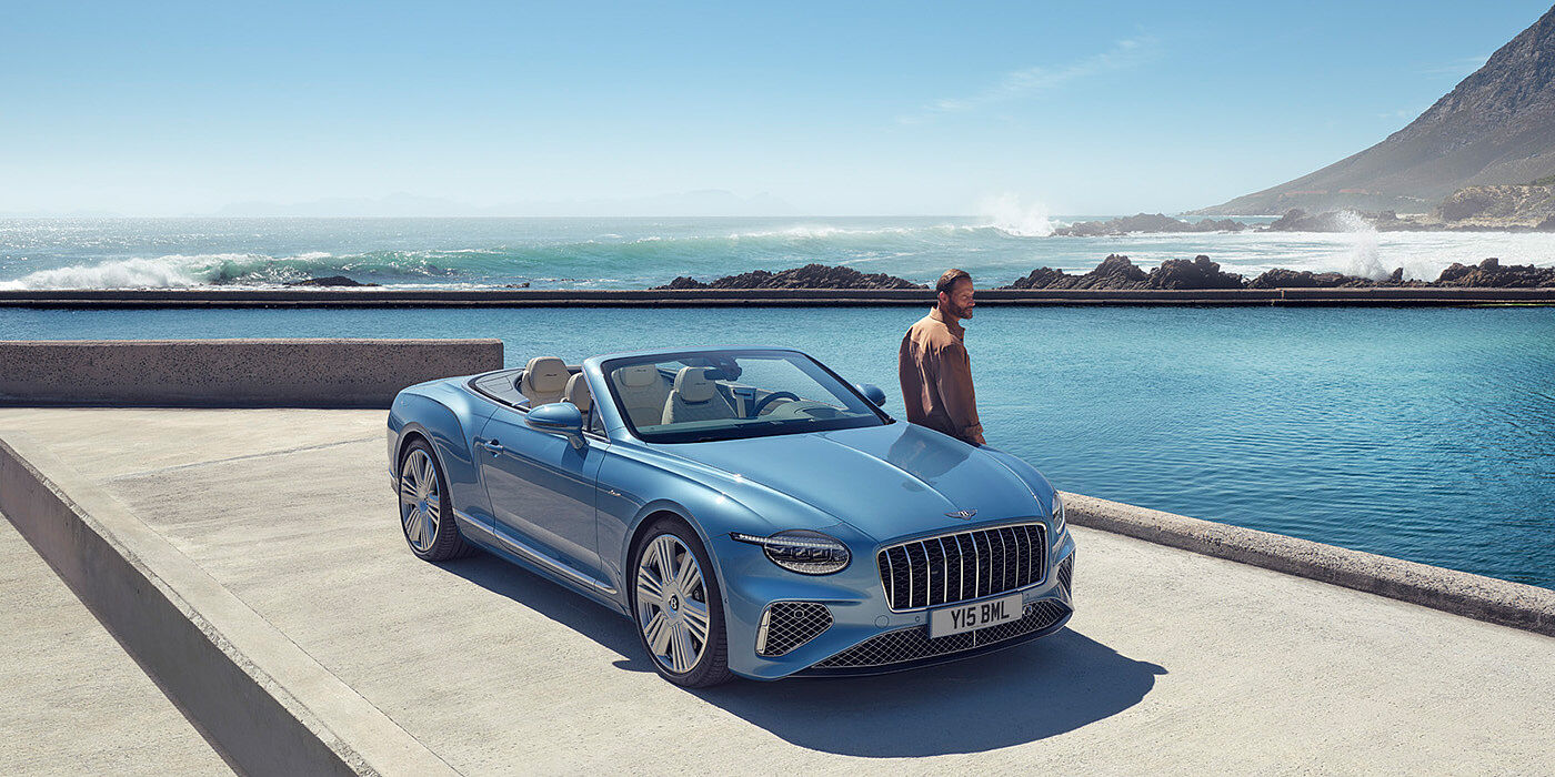 Bentley Lyon New Bentley Continental GTC Azure convertible front view in Light Windsor blue paint with 22 inch ten spoke wheels parked by the sea in the sunshine