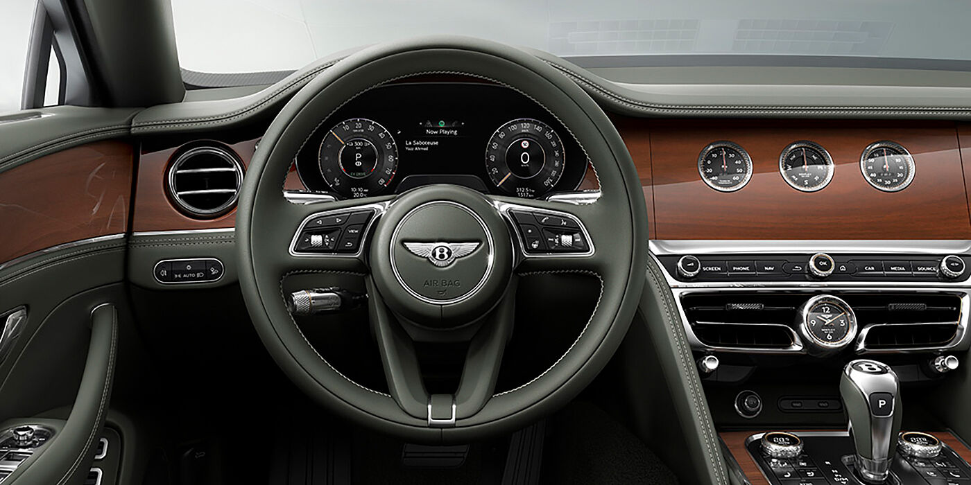 Bentley Lyon New Bentley Flying Spur sedan front cabin in Cumbrian Green hide and Crown Cut walnut veneer showing steering wheel and Rotating Display with three clocks on face