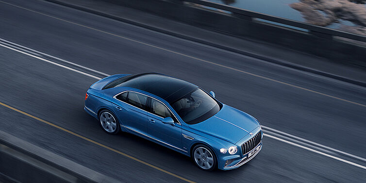 Bentley Lyon New Bentley Flying Spur Azure sedan in Light windsor blue paint by Mulliner, with 22 inch Azure wheels seen from overhead driving dynamically on a country road