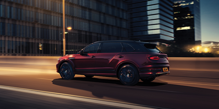 Bentley Lyon Bentley Bentayga Extended Wheelbase Mulliner SUV in Cricket Ball red paint driving dynamically in city at night
